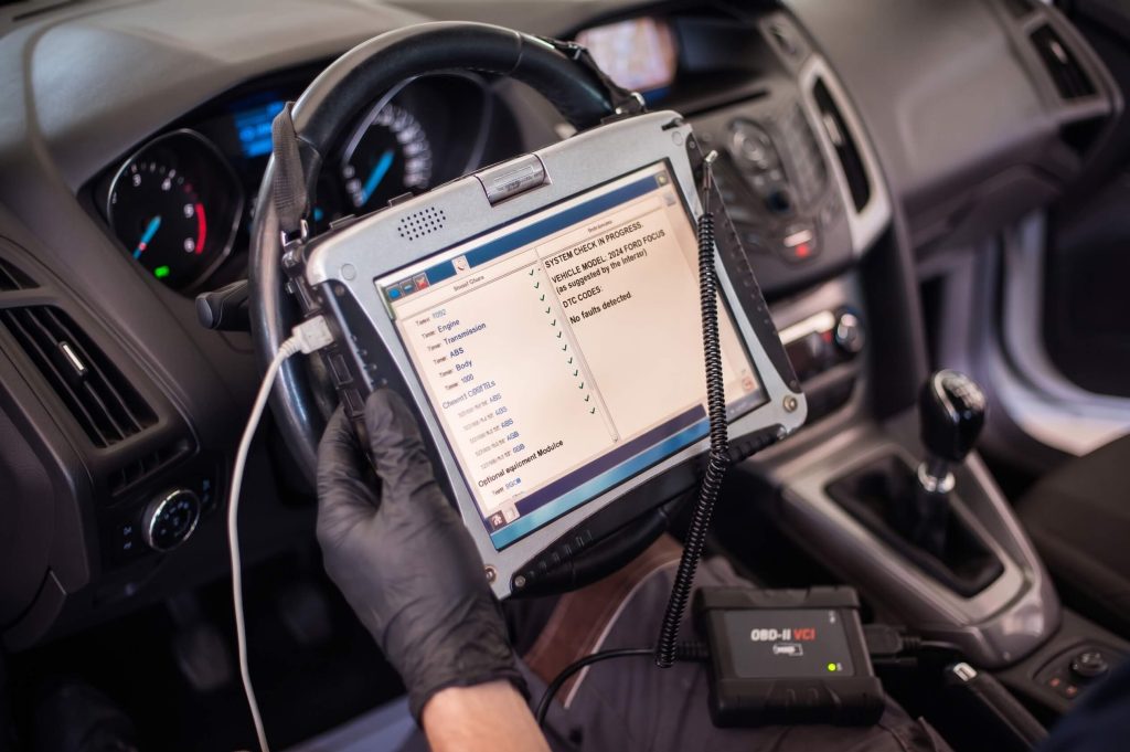 Technicien effectuant un diagnostic électronique automobile à l’aide d’un outil de calibration et d’analyse embarqué.